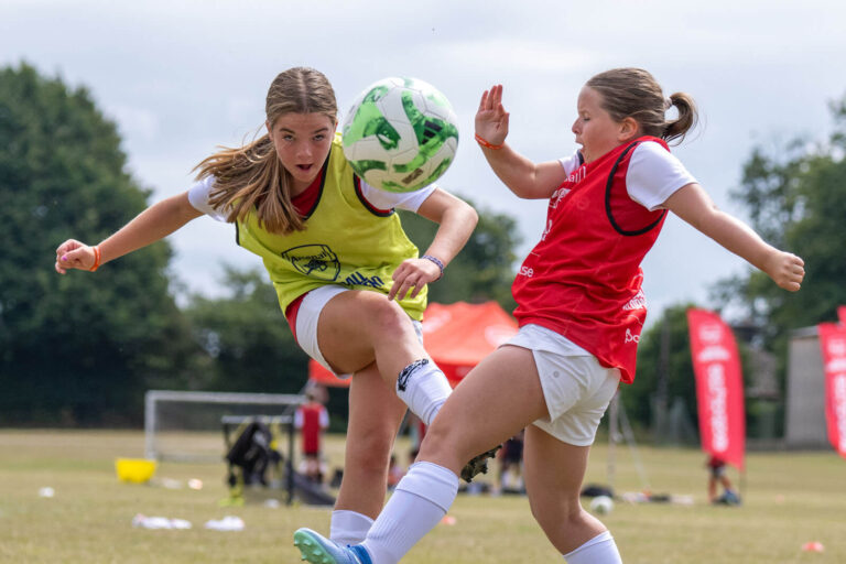 Two girls playing and training together during an Arsenal Football Development summer camp session.
