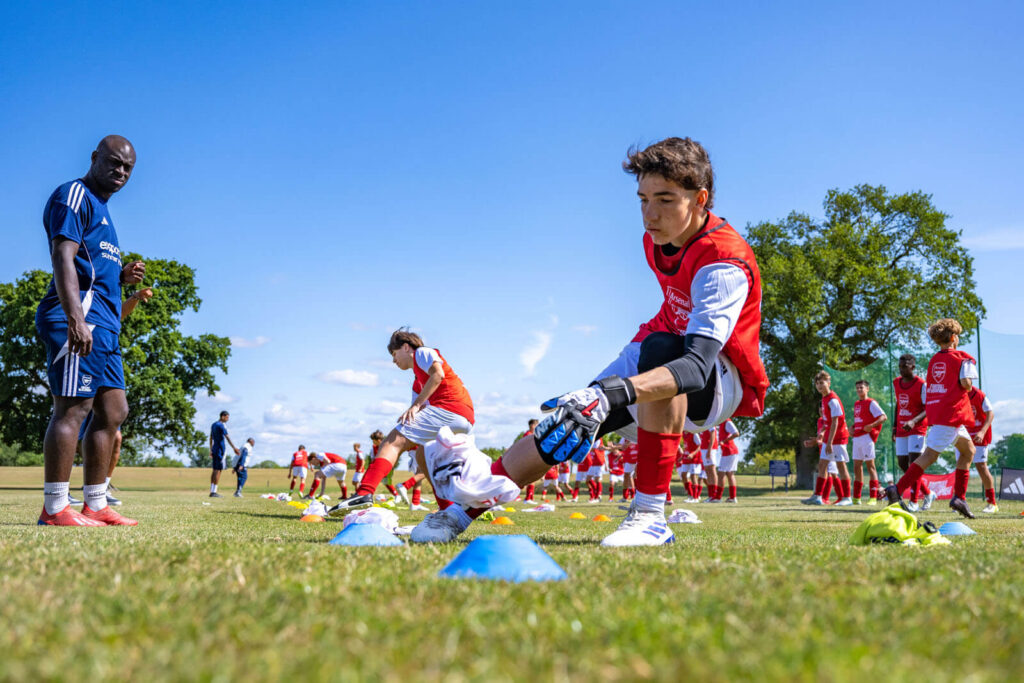 Arsenal camp coach watching a young goalkeeper player performing exercise drills during a training session.