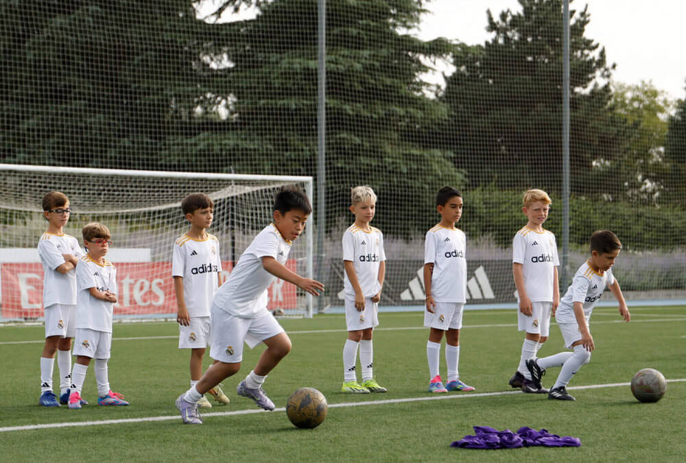 Un grupo de participantes en el Campamento de Día de la Fundación Real Madrid Campus Experience entrenando juntos en un campo de la Ciudad Real Madrid, Valdebebas.